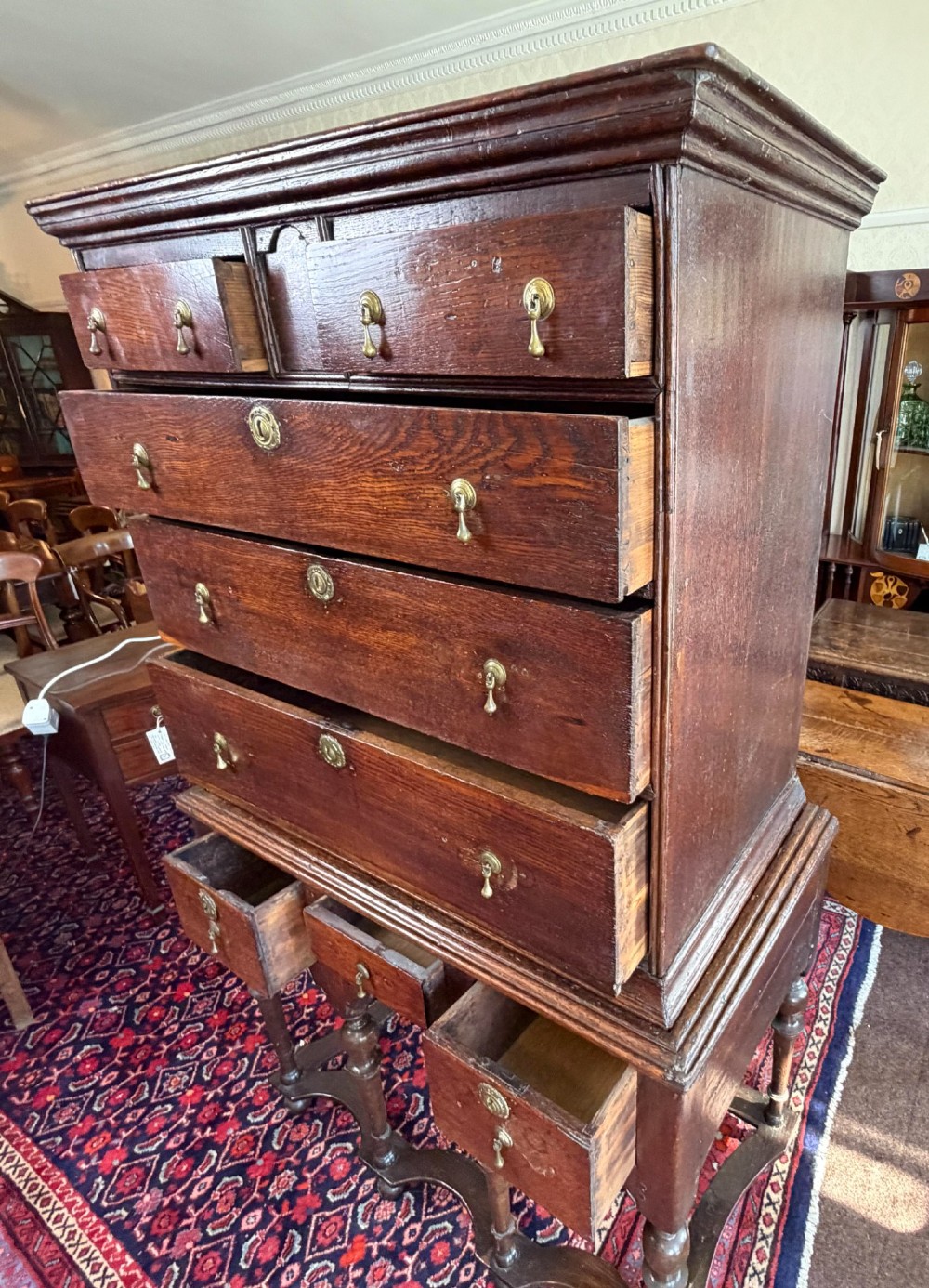 A mid 18th century dark oak chest on stand featuring multiple drawers, brass drop handles, a shaped lower apron, and turned legs with stretchers. View IX