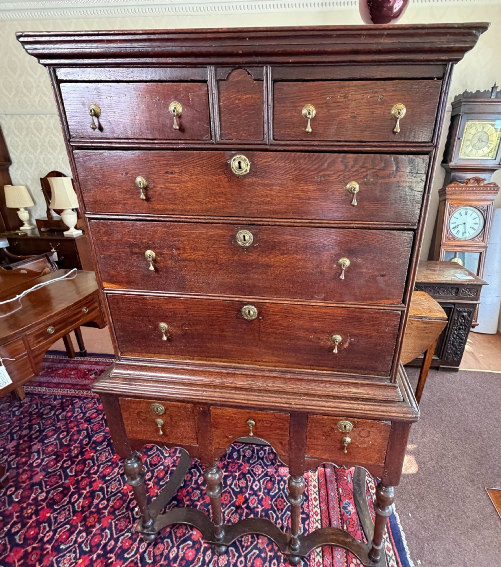 A mid 18th century dark oak chest on stand featuring multiple drawers, brass drop handles, a shaped lower apron, and turned legs with stretchers. View XI