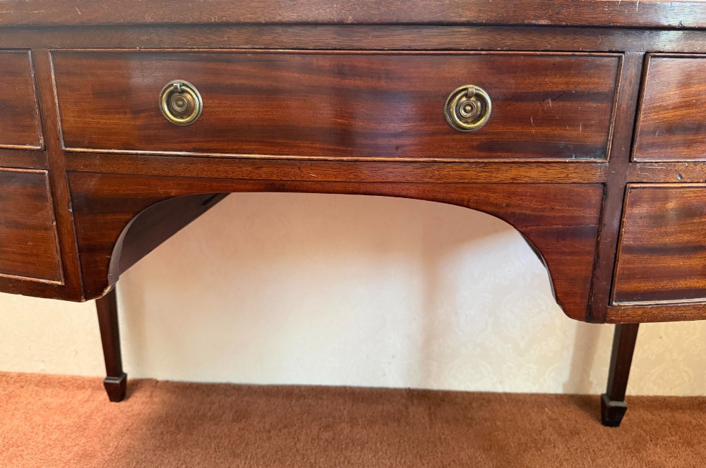 A 19th-century dark mahogany dressing table featuring five drawers with circular brass pull handles, an arched kneehole centre, and square tapered legs. View II