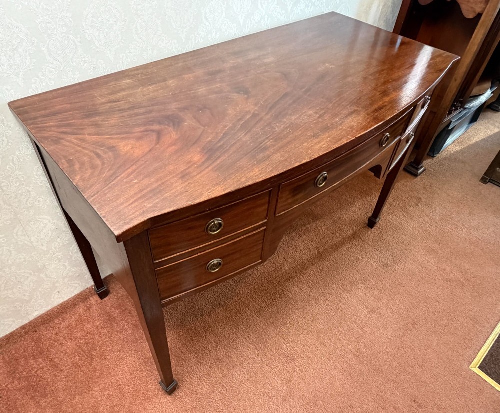 A 19th-century dark mahogany dressing table featuring five drawers with circular brass pull handles, an arched kneehole centre, and square tapered legs. View V