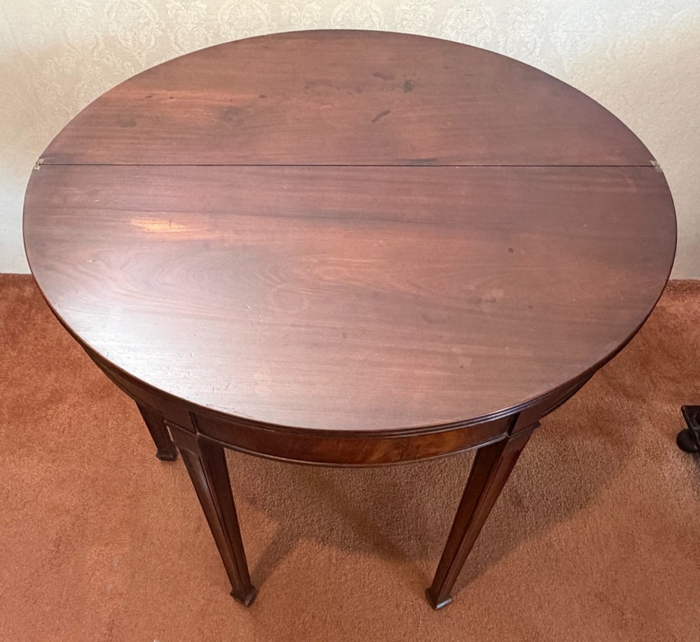 An 18th-century mahogany demi-lune fold-over tea table with tapered reeded legs standing against a wall. View V