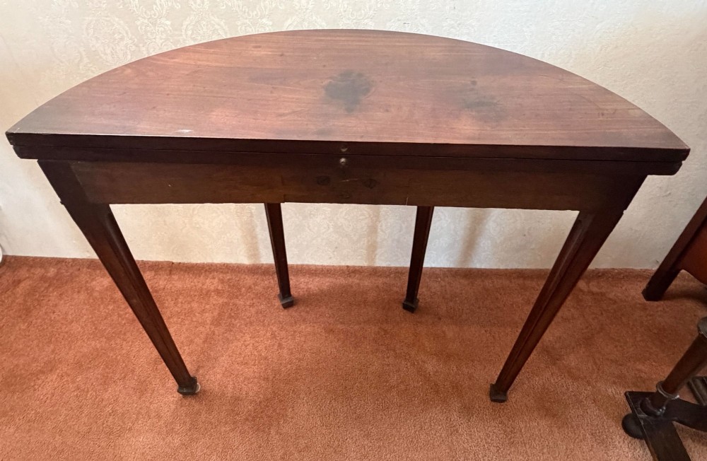 An 18th-century mahogany demi-lune fold-over tea table with tapered reeded legs standing against a wall. View VI