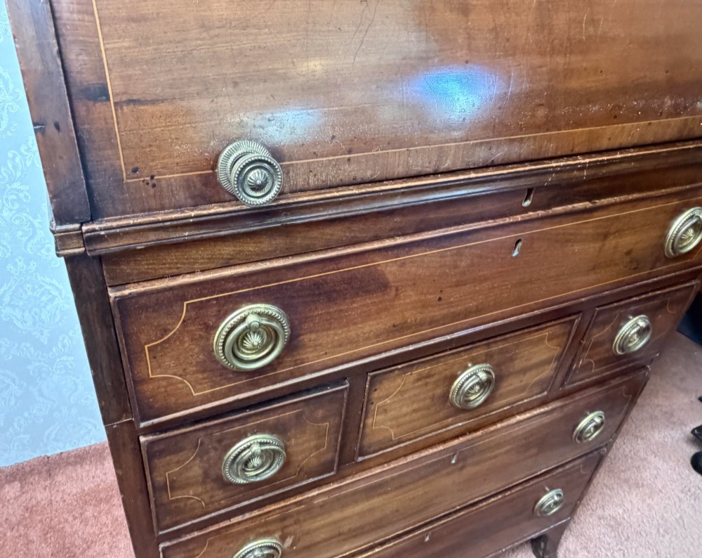 A Georgian mahogany tambour writing desk with boxwood line inlay, circular brass ring handles, and multiple storage drawers beneath a curved roll-top front. View II