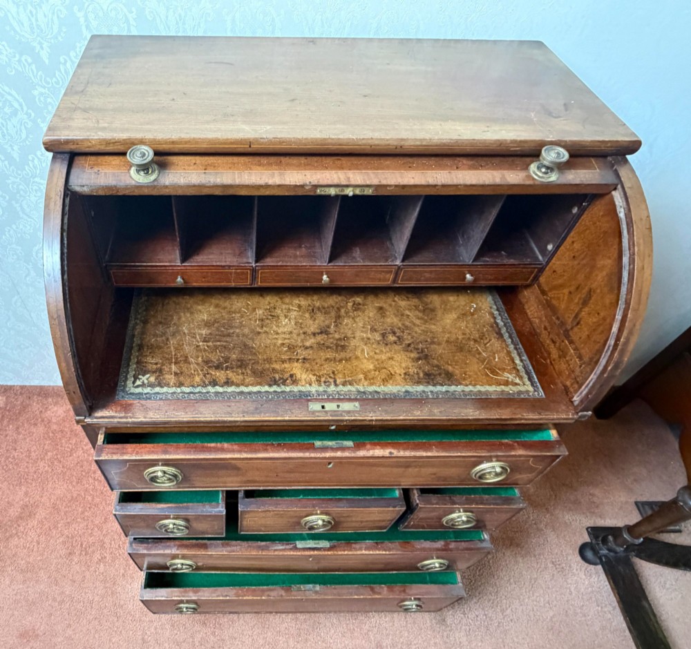 A Georgian mahogany tambour writing desk with boxwood line inlay, circular brass ring handles, and multiple storage drawers beneath a curved roll-top front. View IV