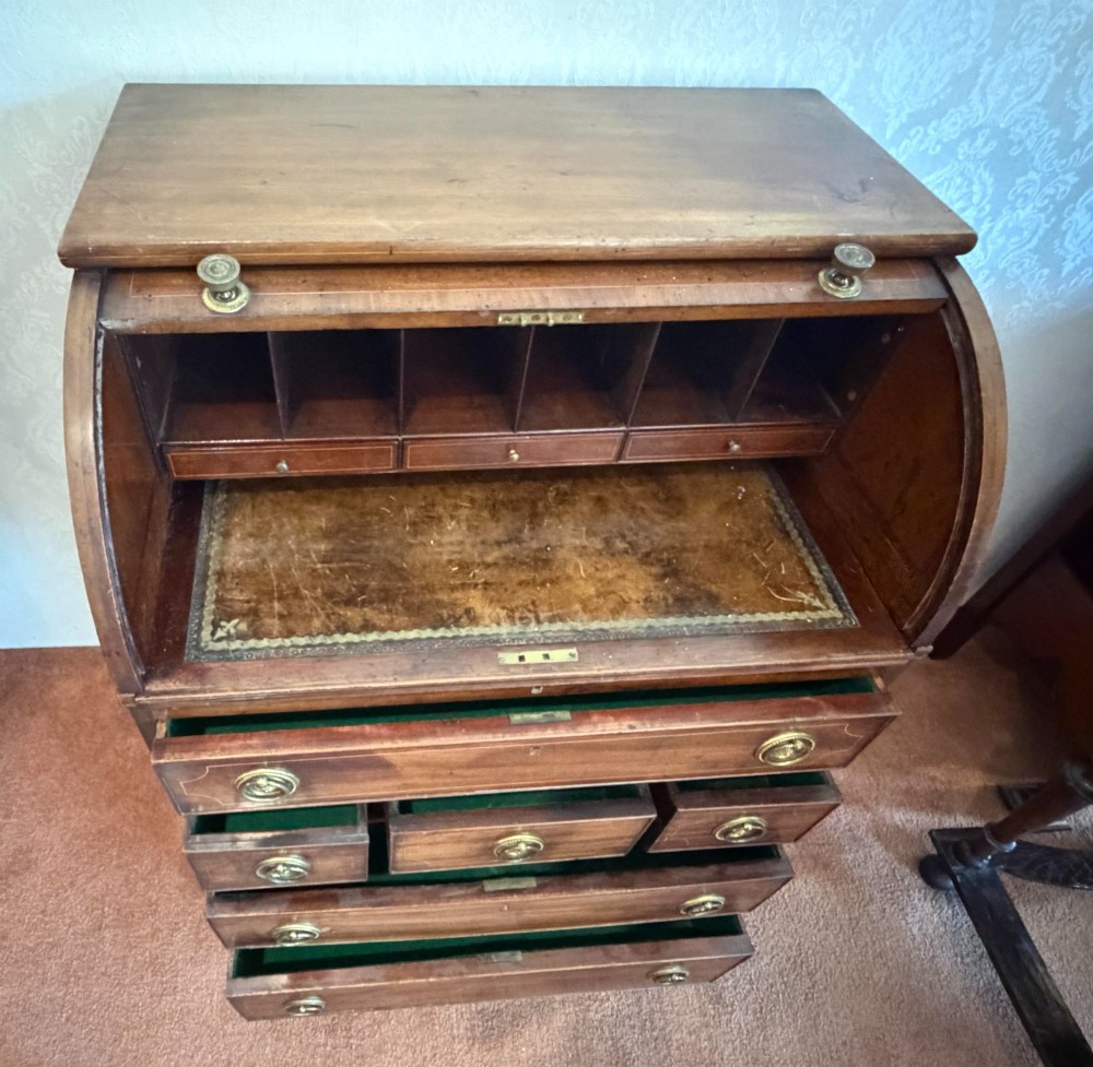 A Georgian mahogany tambour writing desk with boxwood line inlay, circular brass ring handles, and multiple storage drawers beneath a curved roll-top front. View V