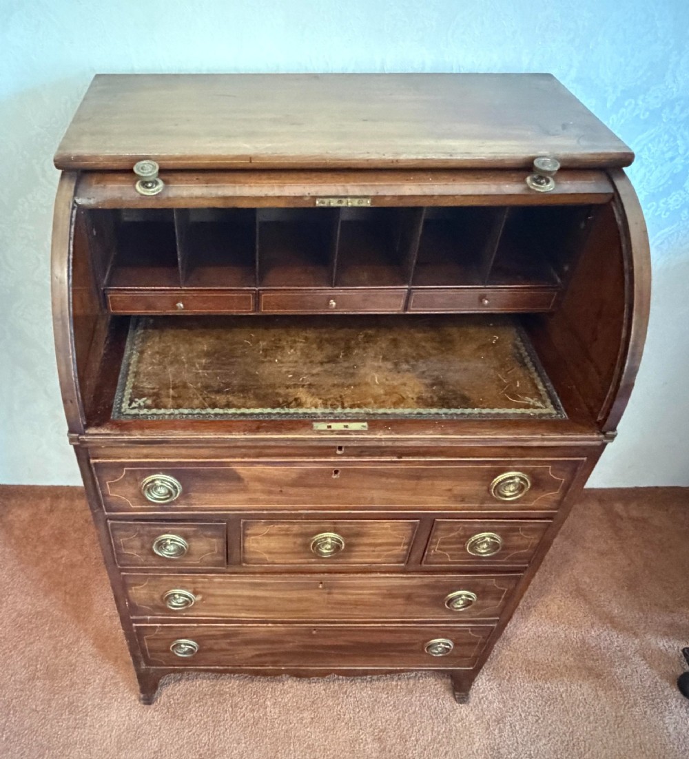 A Georgian mahogany tambour writing desk with boxwood line inlay, circular brass ring handles, and multiple storage drawers beneath a curved roll-top front. View VI