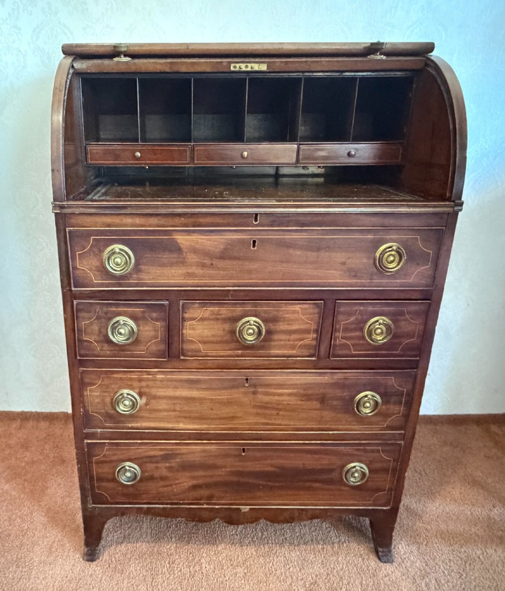 A Georgian mahogany tambour writing desk with boxwood line inlay, circular brass ring handles, and multiple storage drawers beneath a curved roll-top front. View VII