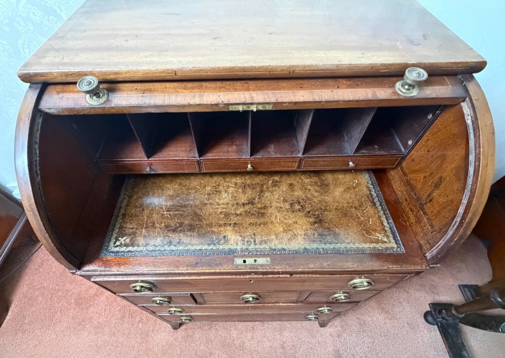 A Georgian mahogany tambour writing desk with boxwood line inlay, circular brass ring handles, and multiple storage drawers beneath a curved roll-top front. View VIII