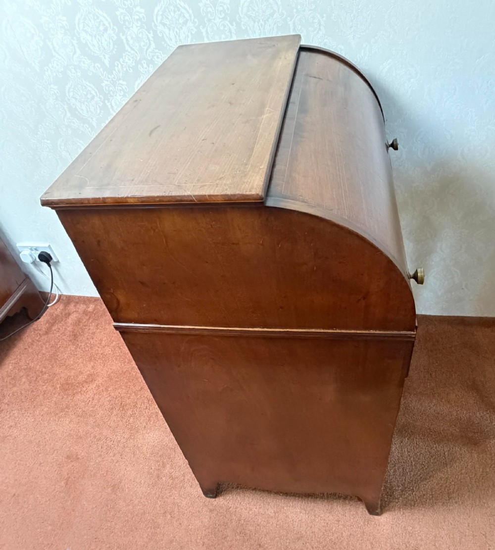 A Georgian mahogany tambour writing desk with boxwood line inlay, circular brass ring handles, and multiple storage drawers beneath a curved roll-top front. View IX