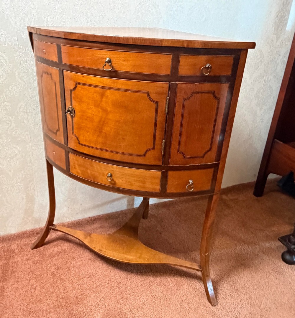 A Georgian satinwood corner washstand with dark timber crossbanding, a central cupboard door, and splayed legs.