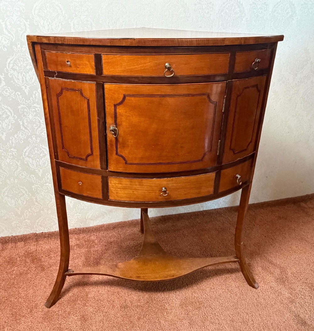 A Georgian satinwood corner washstand with dark timber crossbanding, a central cupboard door, and splayed legs. View II