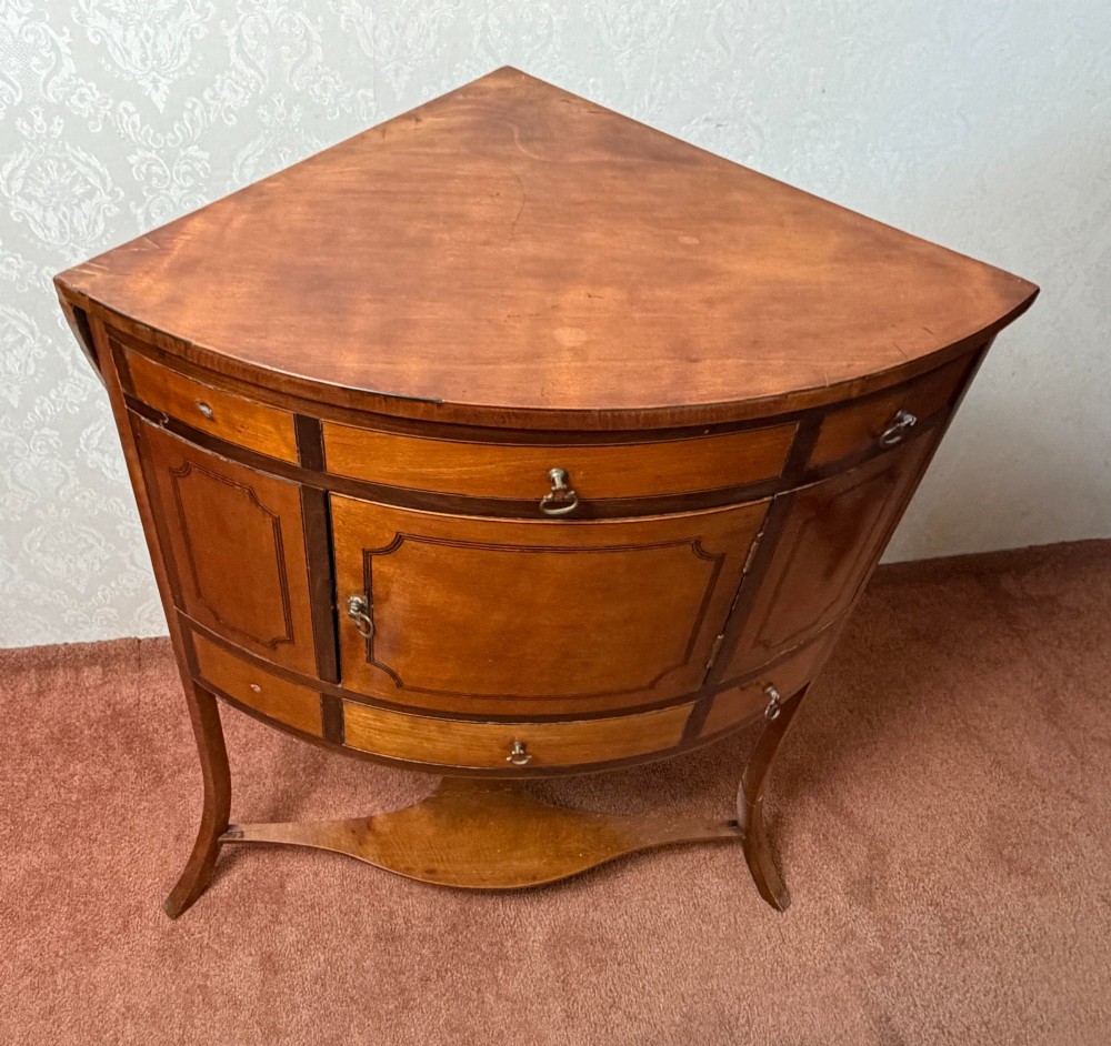 A Georgian satinwood corner washstand with dark timber crossbanding, a central cupboard door, and splayed legs. View III