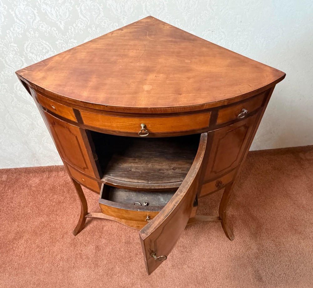 A Georgian satinwood corner washstand with dark timber crossbanding, a central cupboard door, and splayed legs. View IV