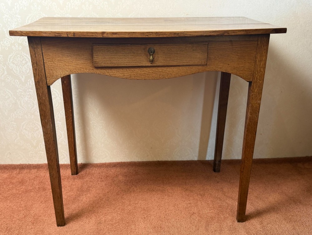 An antique oak side table featuring a single fitted drawer with a brass drop handle, a contoured apron, and four square legs.