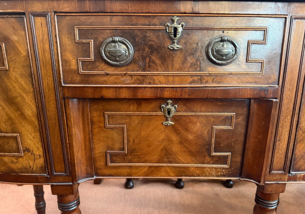 A Regency style mahogany bow-front sideboard featuring geometric string inlay, central drawers flanked by cupboards, brass drop handles, and turned legs. View II