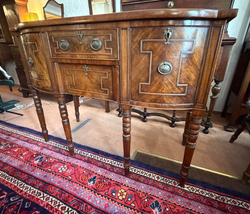 A Regency style mahogany bow-front sideboard featuring geometric string inlay, central drawers flanked by cupboards, brass drop handles, and turned legs. View III