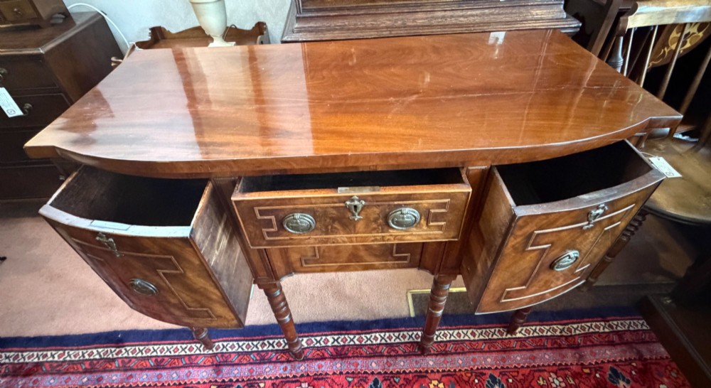 A Regency style mahogany bow-front sideboard featuring geometric string inlay, central drawers flanked by cupboards, brass drop handles, and turned legs. View IV