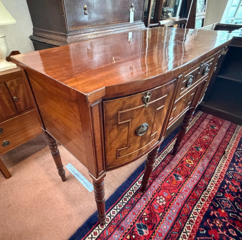 A Regency style mahogany bow-front sideboard featuring geometric string inlay, central drawers flanked by cupboards, brass drop handles, and turned legs. View V