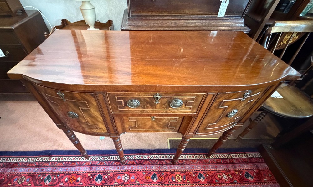A Regency style mahogany bow-front sideboard featuring geometric string inlay, central drawers flanked by cupboards, brass drop handles, and turned legs. View VI