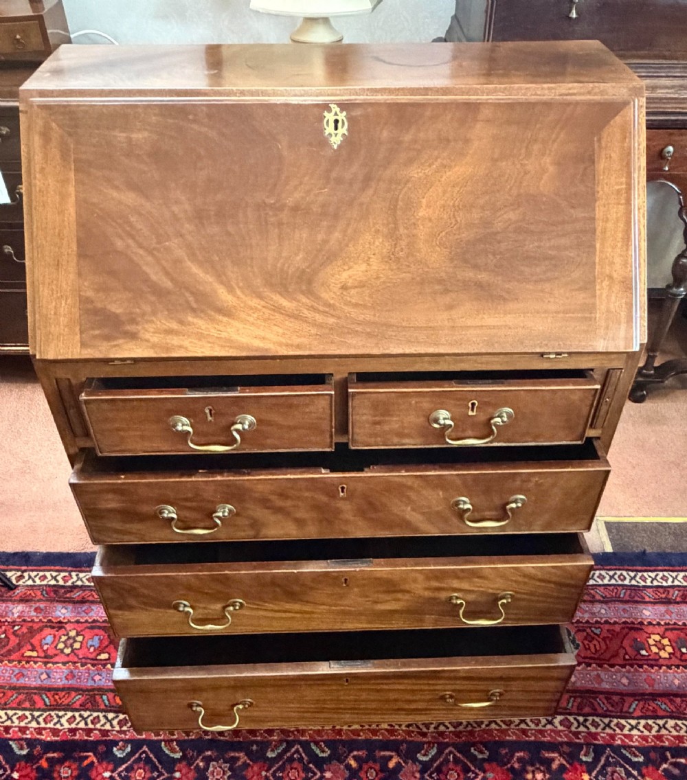 A George III mahogany bureau featuring a slant-front writing slope above two short and three long drawers with brass swan-neck handles, resting on bracket feet. View II