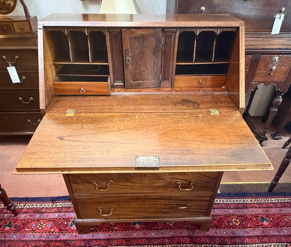A George III mahogany bureau featuring a slant-front writing slope above two short and three long drawers with brass swan-neck handles, resting on bracket feet. View III