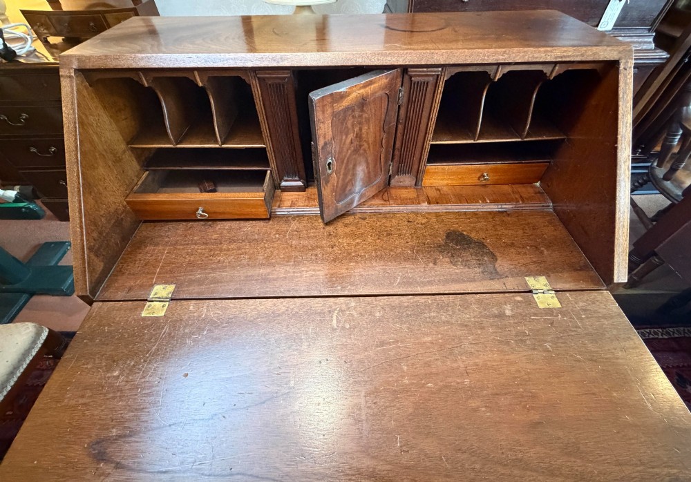 A George III mahogany bureau featuring a slant-front writing slope above two short and three long drawers with brass swan-neck handles, resting on bracket feet. View IV