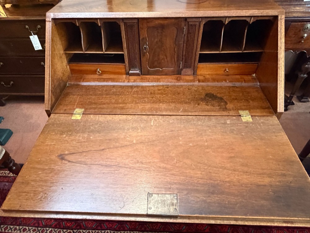 A George III mahogany bureau featuring a slant-front writing slope above two short and three long drawers with brass swan-neck handles, resting on bracket feet. View V