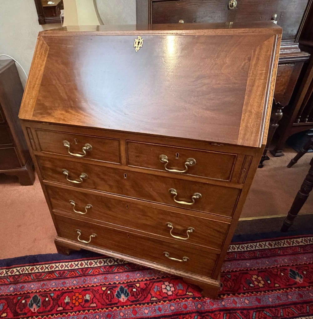 A George III mahogany bureau featuring a slant-front writing slope above two short and three long drawers with brass swan-neck handles, resting on bracket feet. View VII