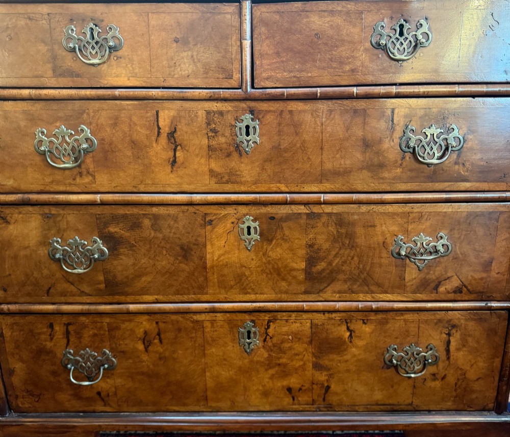 An antique burr walnut chest of drawers featuring two short over three long drawers with ornate brass drop handles and bracket feet. View III