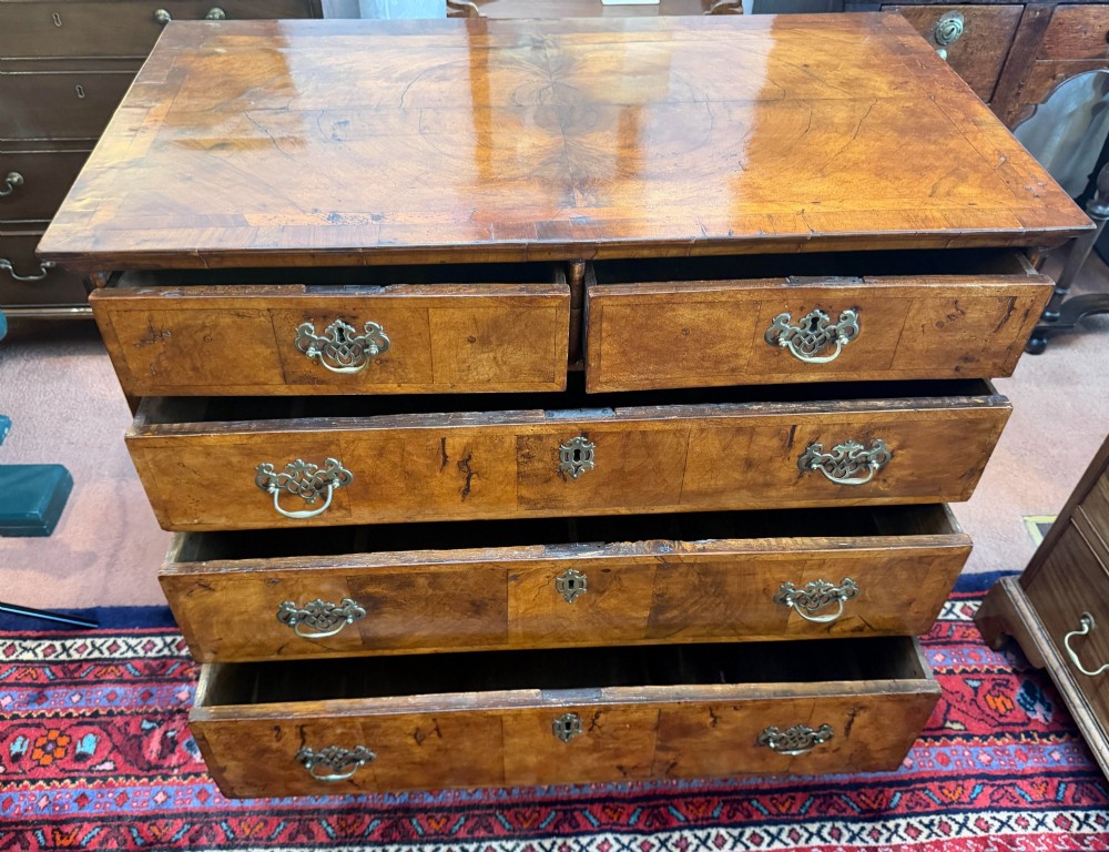 An antique burr walnut chest of drawers featuring two short over three long drawers with ornate brass drop handles and bracket feet. View IV