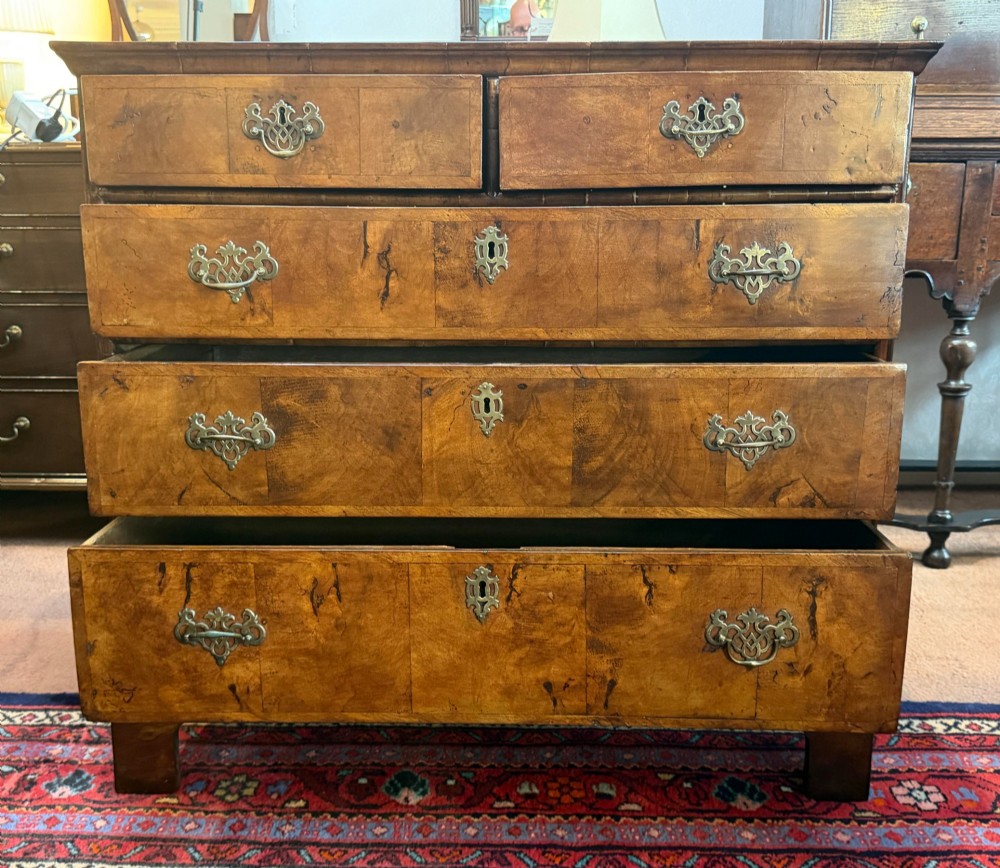 An antique burr walnut chest of drawers featuring two short over three long drawers with ornate brass drop handles and bracket feet. View V