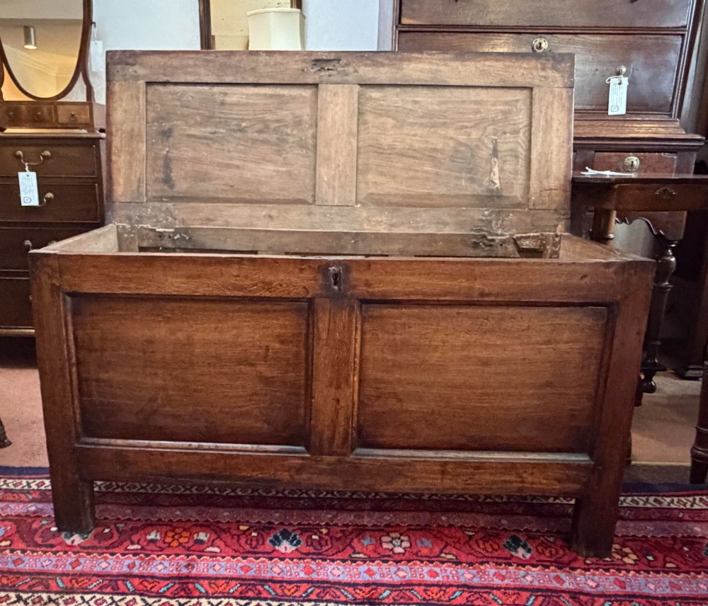 An antique oak coffer featuring a hinged rectangular top, two recessed front panels, and a central iron keyhole escutcheon resting on short block feet. View II