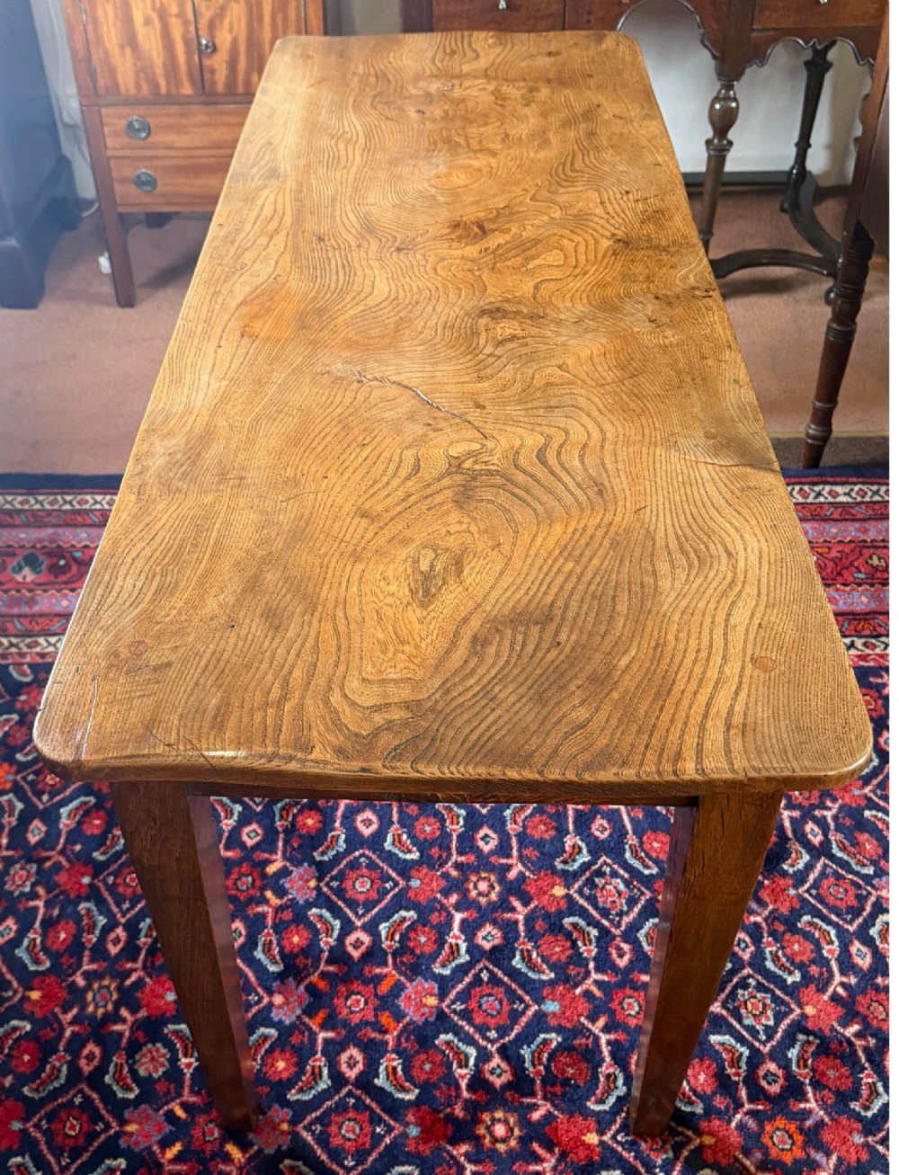 A rectangular antique wooden farmhouse table featuring a highly figured timber grain top supported by four square tapered legs. View VII