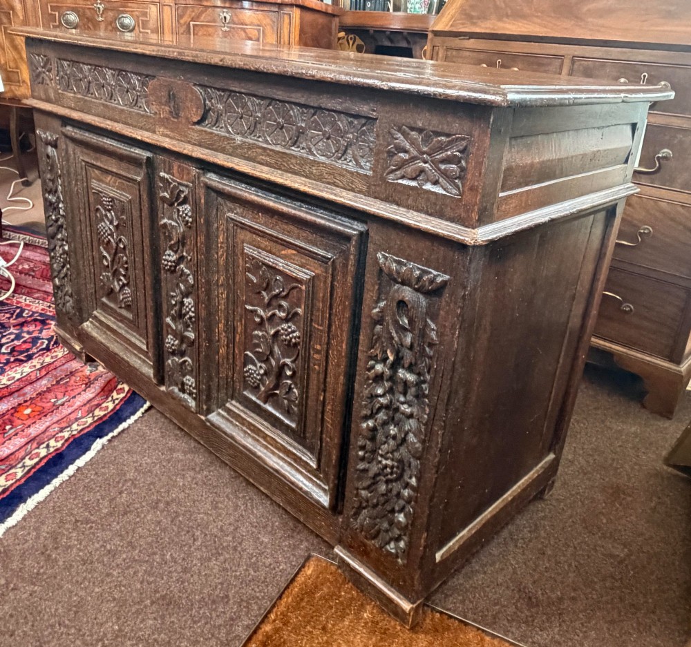 A 17th-century dark oak coffer featuring hand-carved vine and grape motifs across three front panels. View II