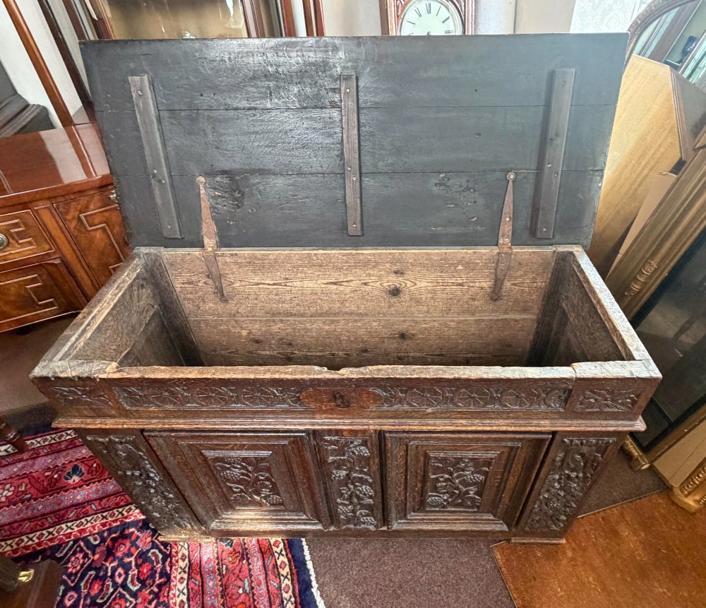 A 17th-century dark oak coffer featuring hand-carved vine and grape motifs across three front panels. View III