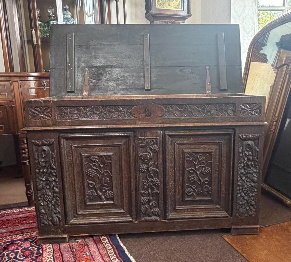 A 17th-century dark oak coffer featuring hand-carved vine and grape motifs across three front panels. View IV