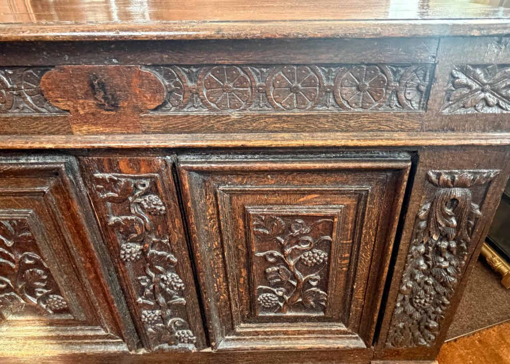 A 17th-century dark oak coffer featuring hand-carved vine and grape motifs across three front panels. View VI