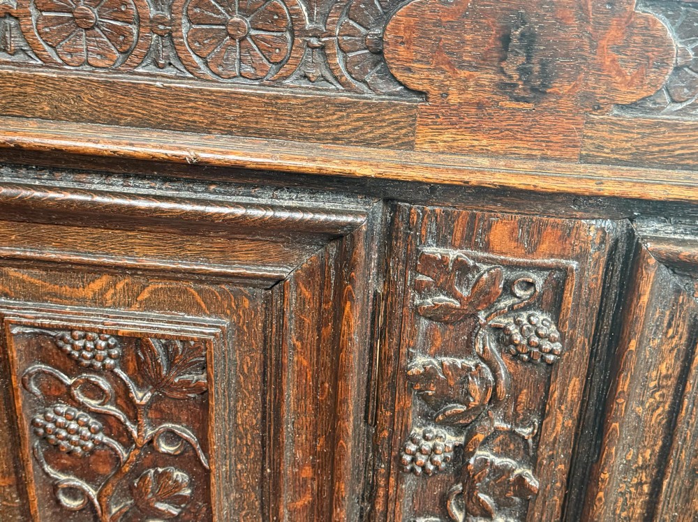 A 17th-century dark oak coffer featuring hand-carved vine and grape motifs across three front panels. View VII