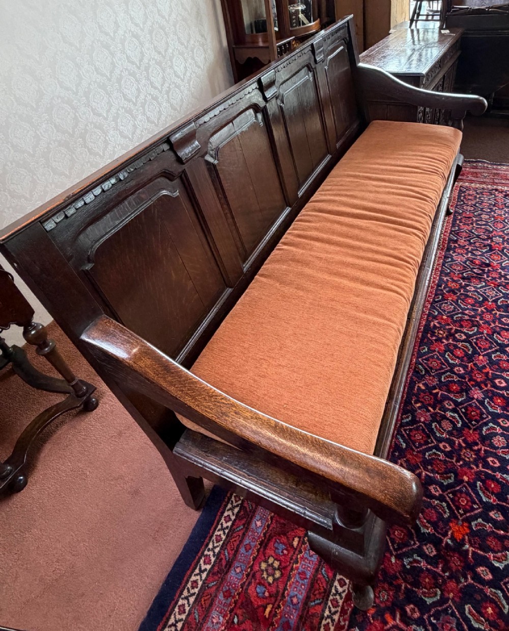 An eighteenth-century dark oak pub settle featuring a four-panel backrest, curved armrests, cabriole legs, and a fitted terracotta seat cushion. View II