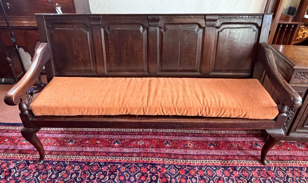 An eighteenth-century dark oak pub settle featuring a four-panel backrest, curved armrests, cabriole legs, and a fitted terracotta seat cushion. View III