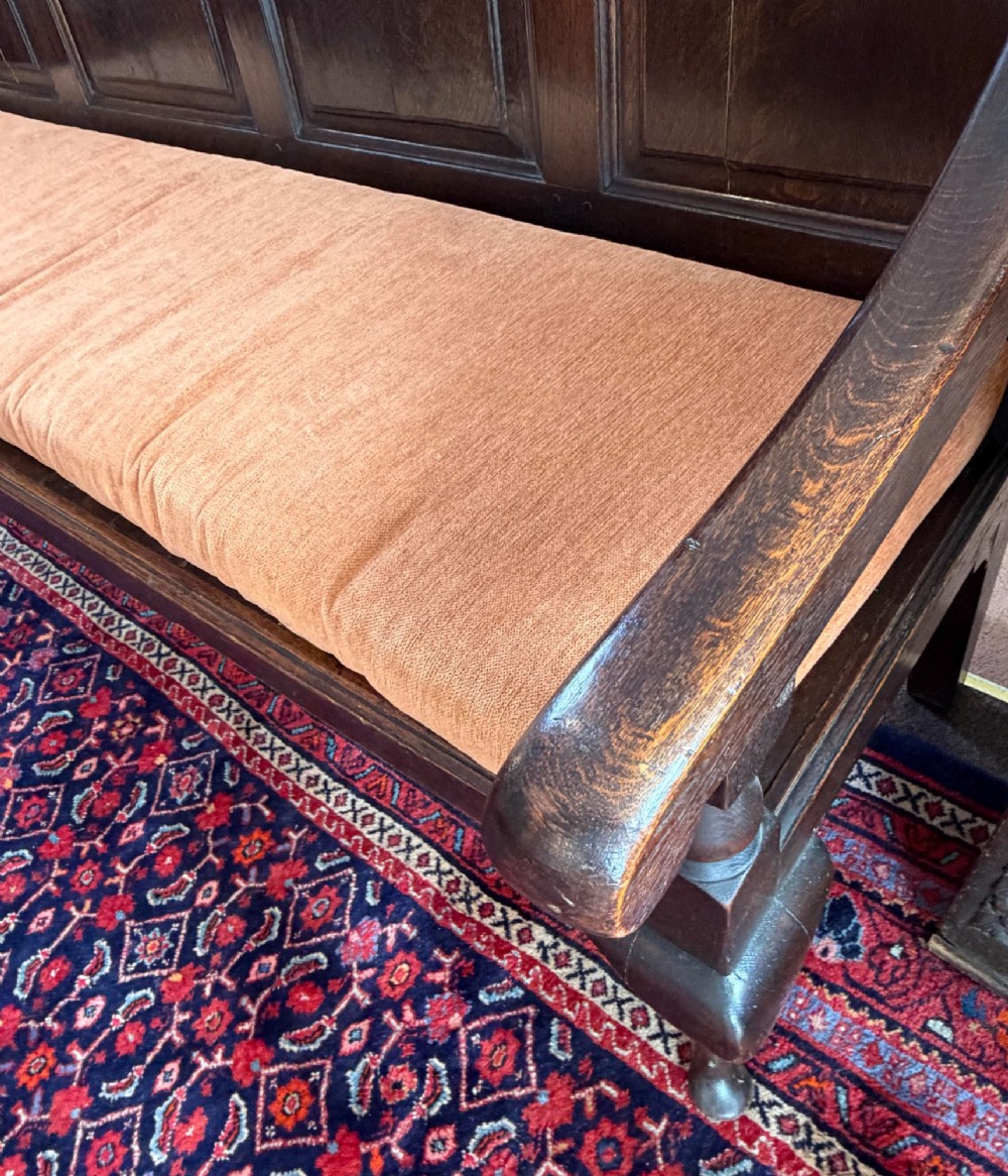 An eighteenth-century dark oak pub settle featuring a four-panel backrest, curved armrests, cabriole legs, and a fitted terracotta seat cushion. View IV