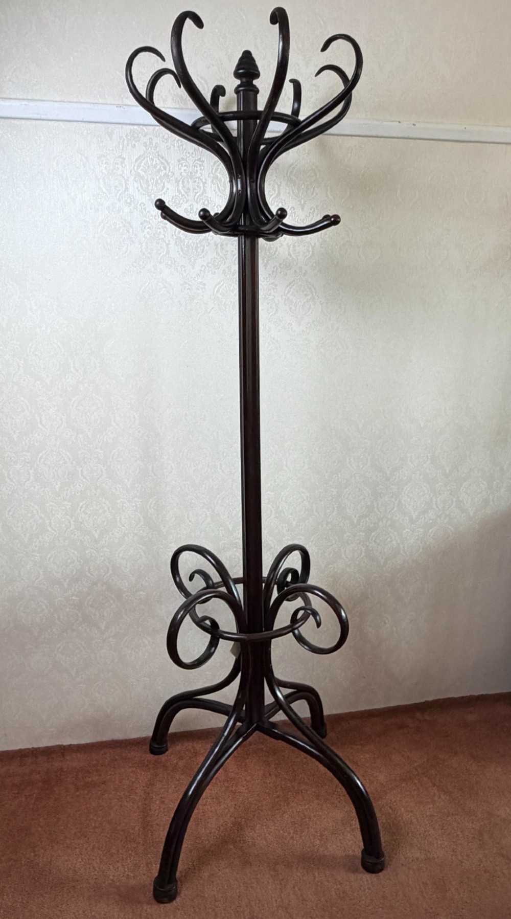 A tall dark brown bentwood coat stand featuring curved upper hooks, a lower umbrella ring, and splayed legs with a turned central post. View II