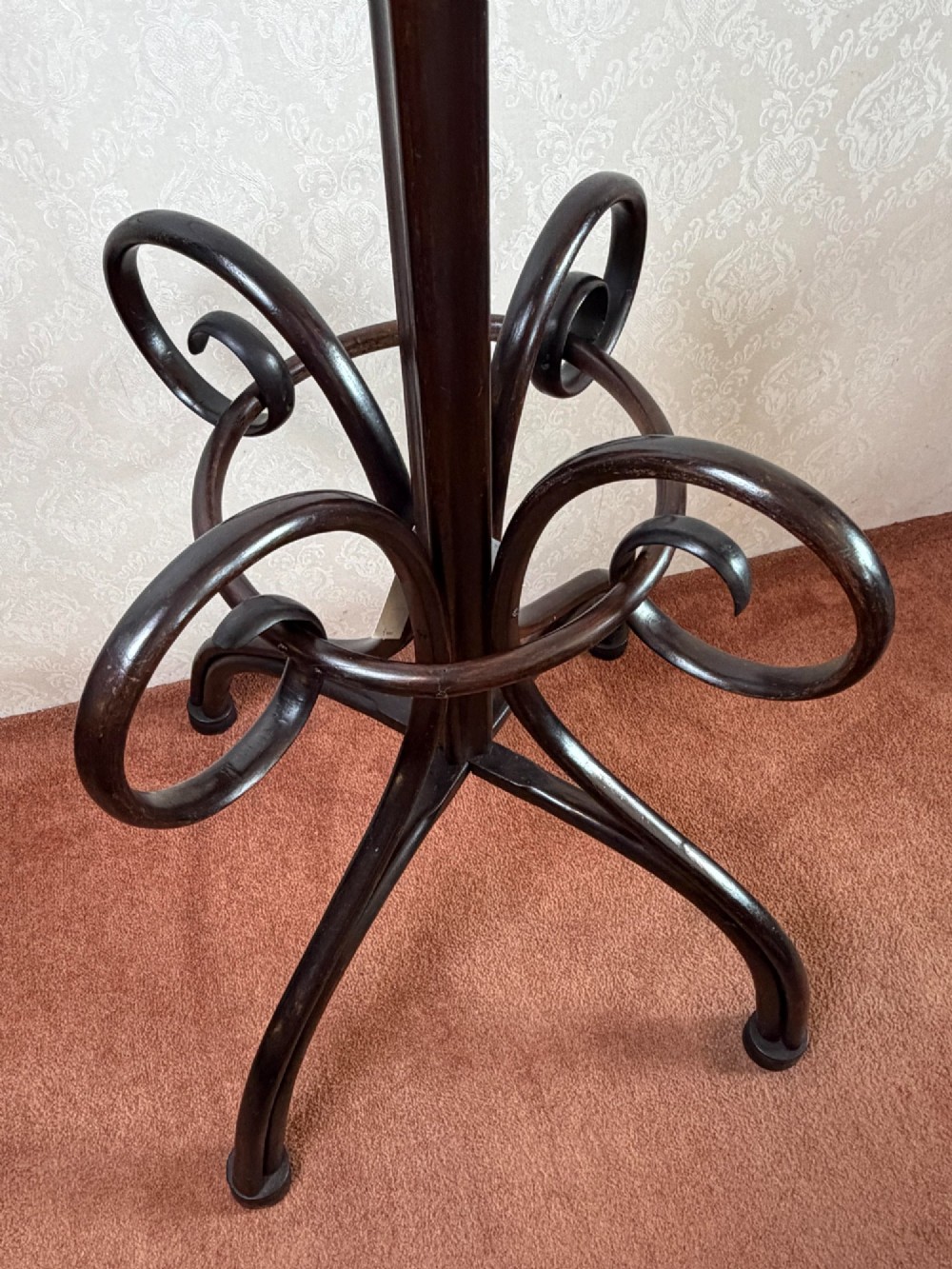 A tall dark brown bentwood coat stand featuring curved upper hooks, a lower umbrella ring, and splayed legs with a turned central post. View III