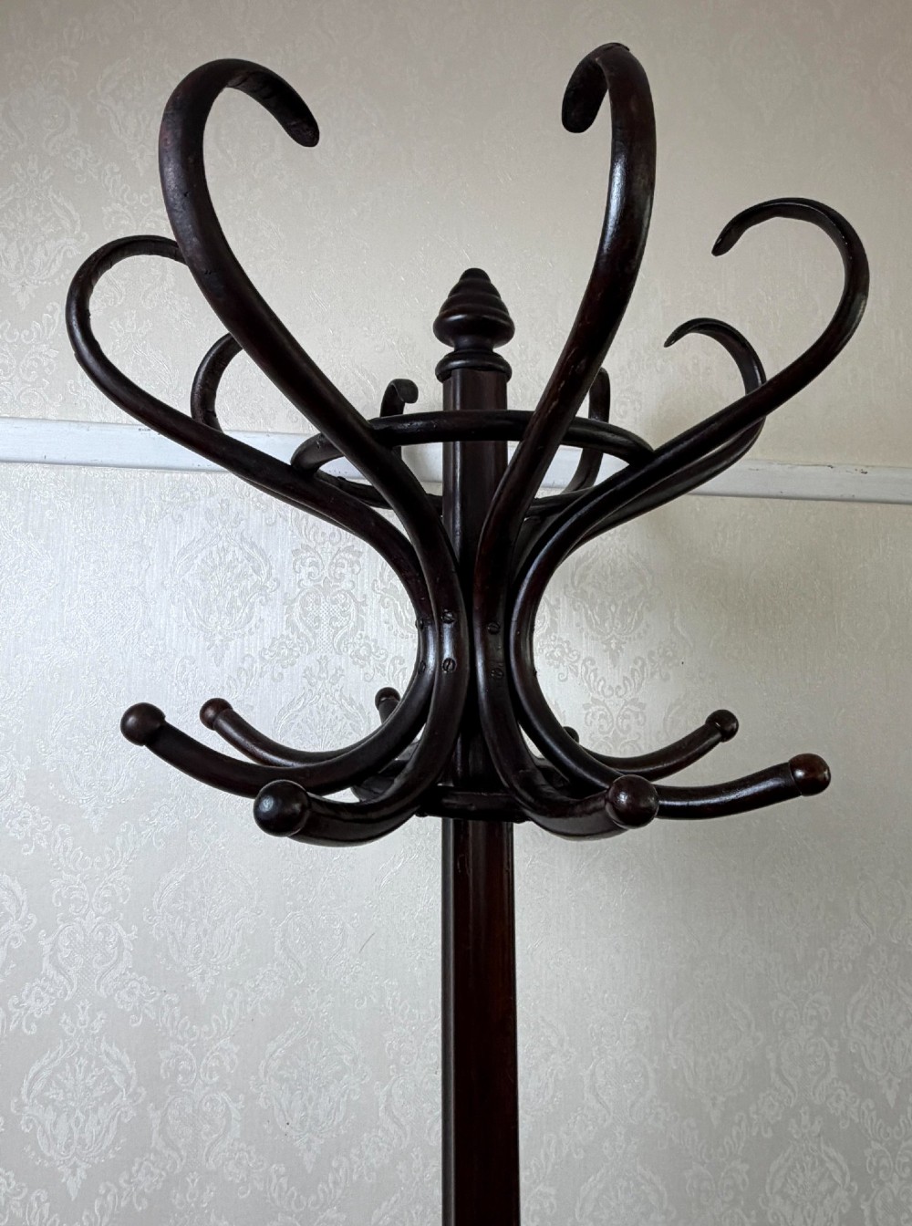 A tall dark brown bentwood coat stand featuring curved upper hooks, a lower umbrella ring, and splayed legs with a turned central post. View IV