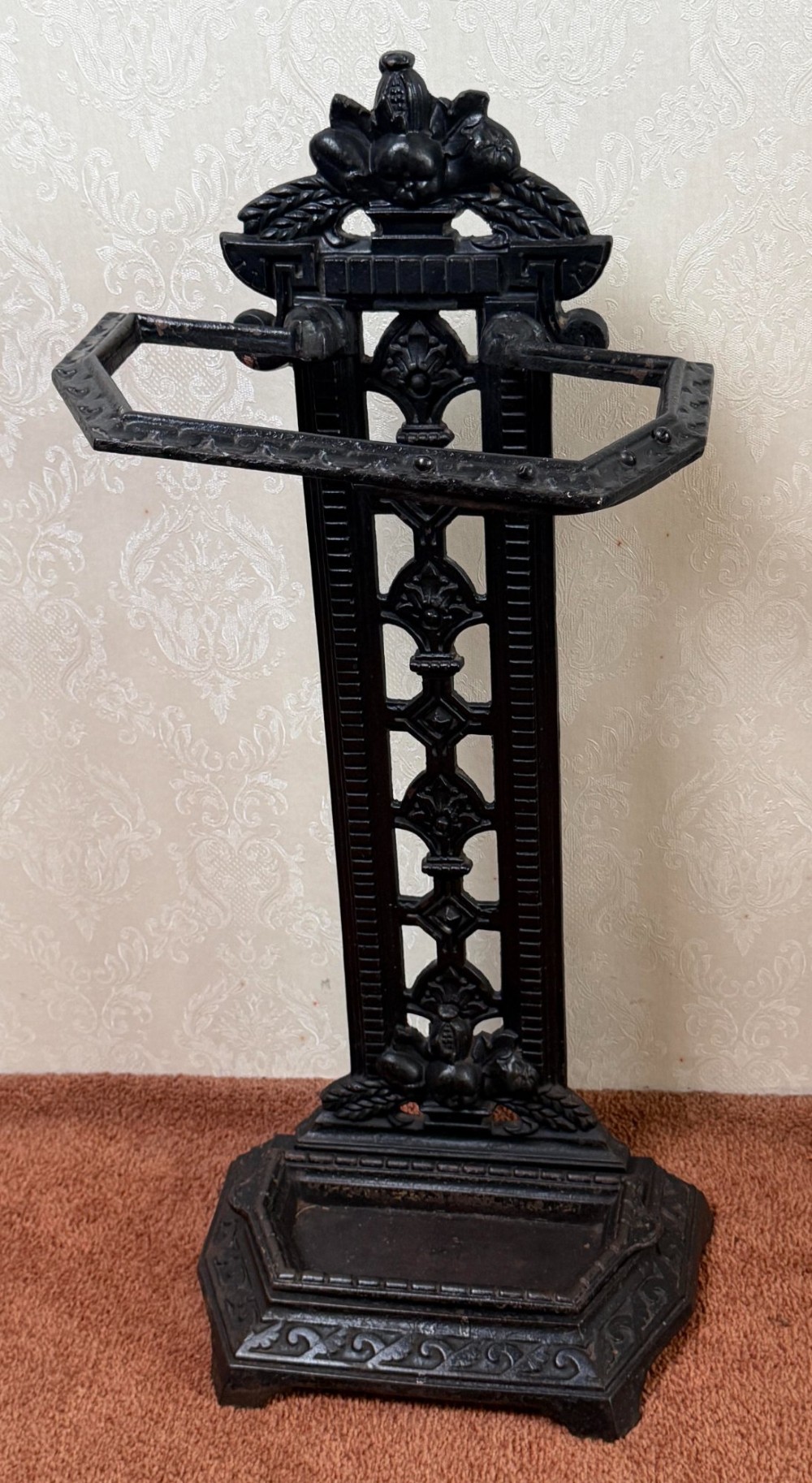 A Victorian black cast iron umbrella stand featuring a foliate crest, an openwork backplate, a retaining rail, and a drip tray base.