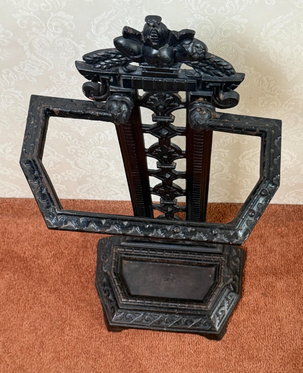 A Victorian black cast iron umbrella stand featuring a foliate crest, an openwork backplate, a retaining rail, and a drip tray base. View II