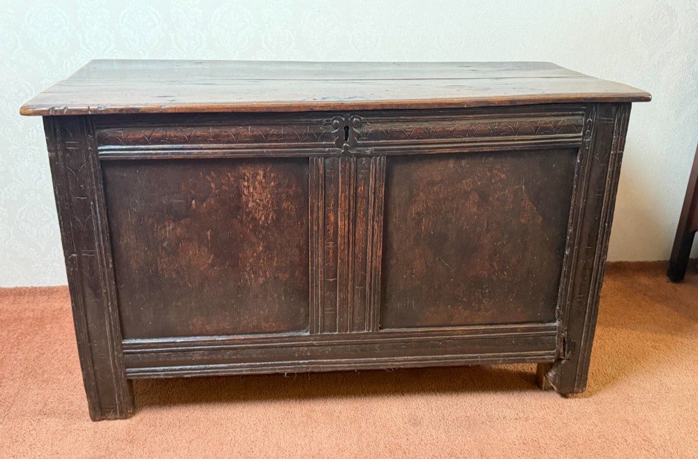 A late seventeenth-century dark oak coffer featuring carved frieze detailing, two front panels, and a hinged plank top.