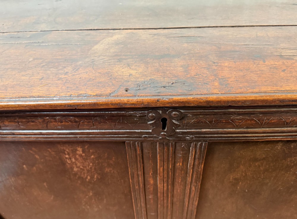 A late seventeenth-century dark oak coffer featuring carved frieze detailing, two front panels, and a hinged plank top. View II