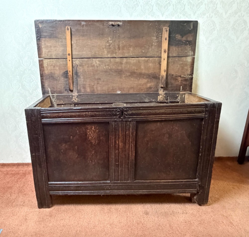 A late seventeenth-century dark oak coffer featuring carved frieze detailing, two front panels, and a hinged plank top. View III