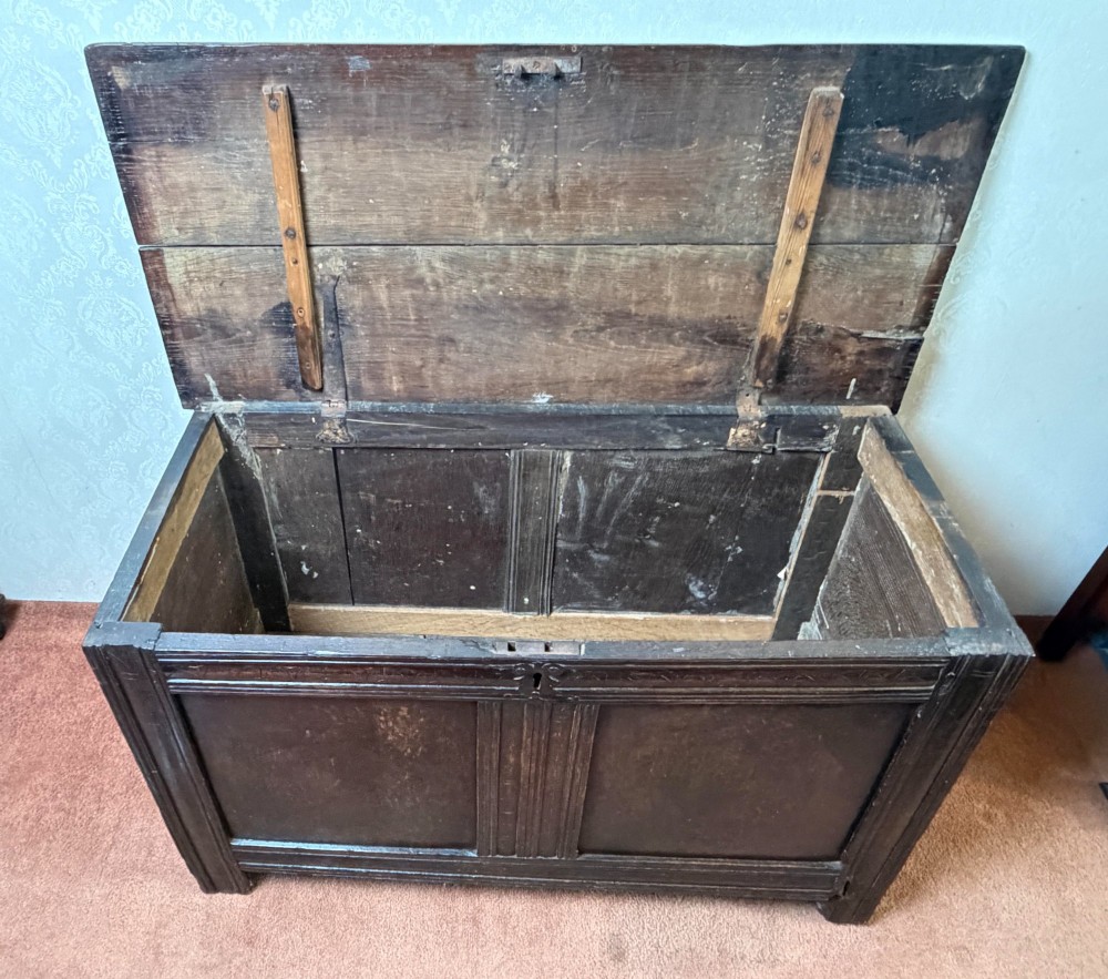 A late seventeenth-century dark oak coffer featuring carved frieze detailing, two front panels, and a hinged plank top. View IV